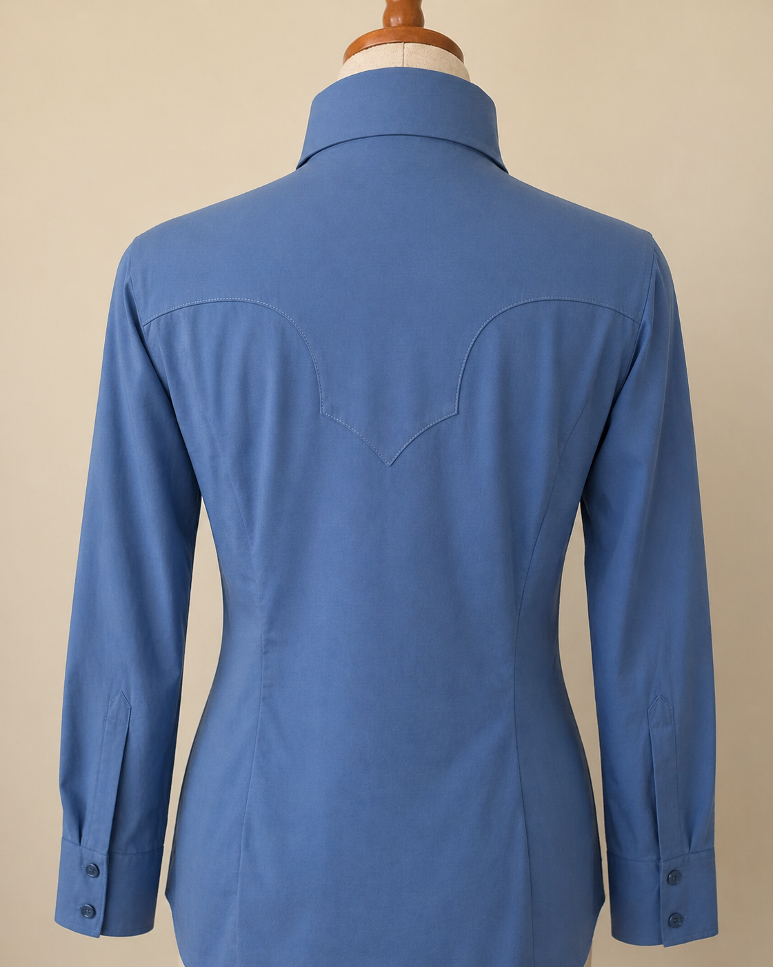A blue long-sleeve western-style shirt shown from the back on a dress form, featuring a collar, button cuffs, and a curved yoke detail.