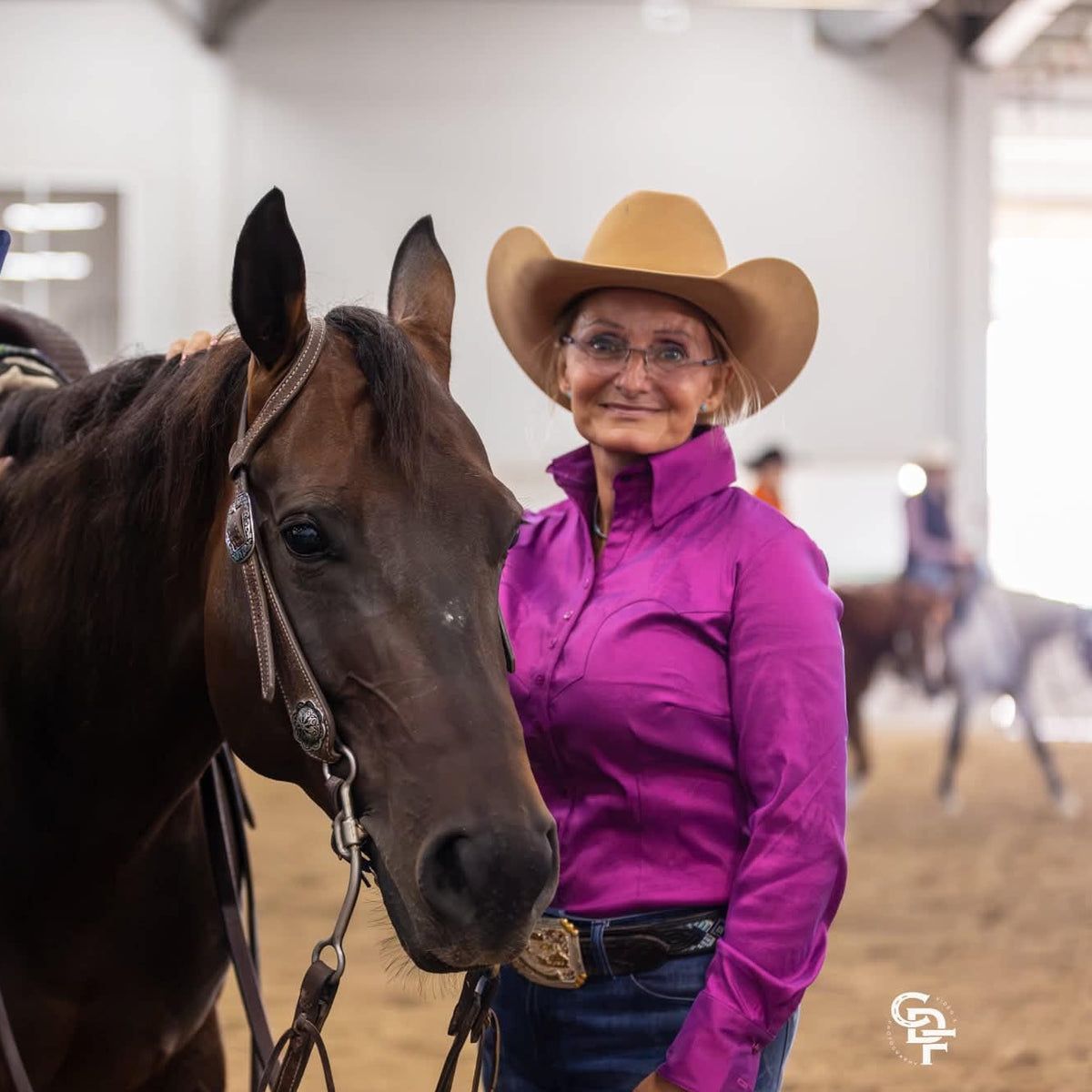 woman wearing purple stretch taffeta western shirt wearing a trophy buckle, standing next to her horse