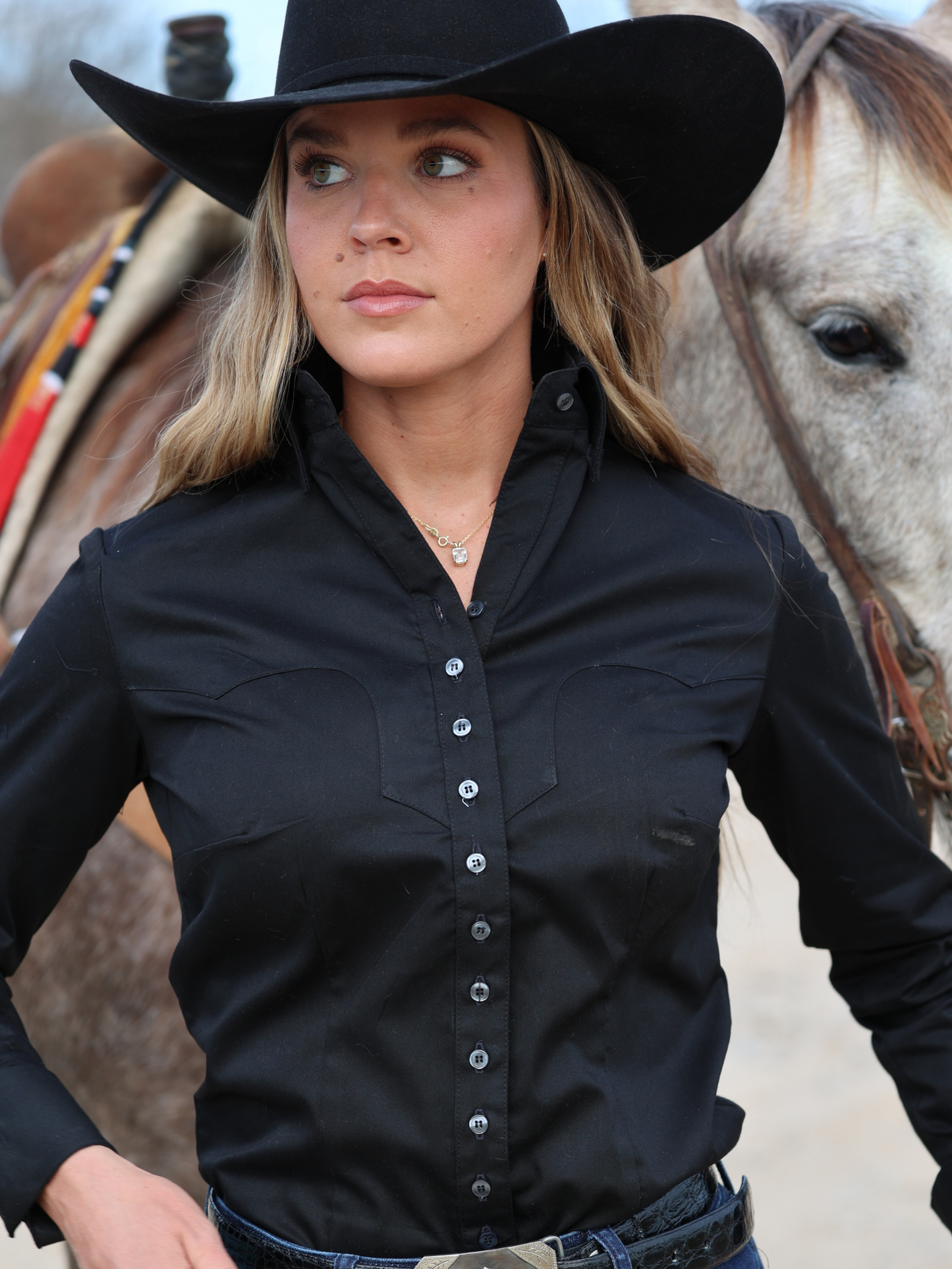 Woman wearing a black cowboy hat and shirt with a horse in the background