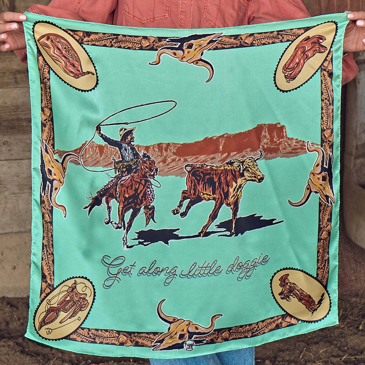 Get Along Little Doggie Wild Rag held outstretched showing full cowboy roping longhorn design in mint, tan, and brown
