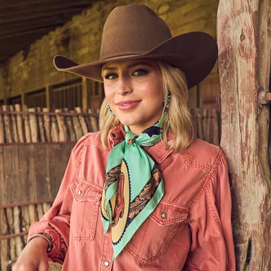 Get Along Little Doggie Wild Rag tied loosely at neckline with concho slide over coral denim shirt and brown felt cowboy hat