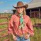 Get Along Little Doggie Wild Rag knotted at chest over coral western shirt with turquoise concho belt, silver cuffs, and brown cowboy hat at ranch gate