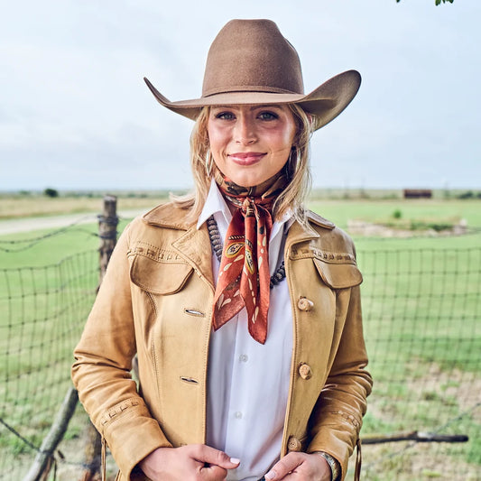 Happy Trails Wild Rag tied loosely at neckline over white shirt and tan fringe leather jacket with brown felt cowboy hat