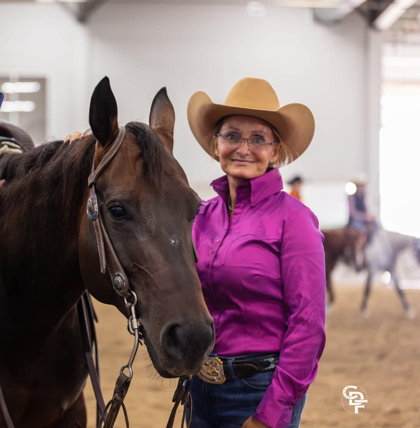 woman wearing purple stretch taffeta western shirt wearing a trophy buckle, standing next to her horse
